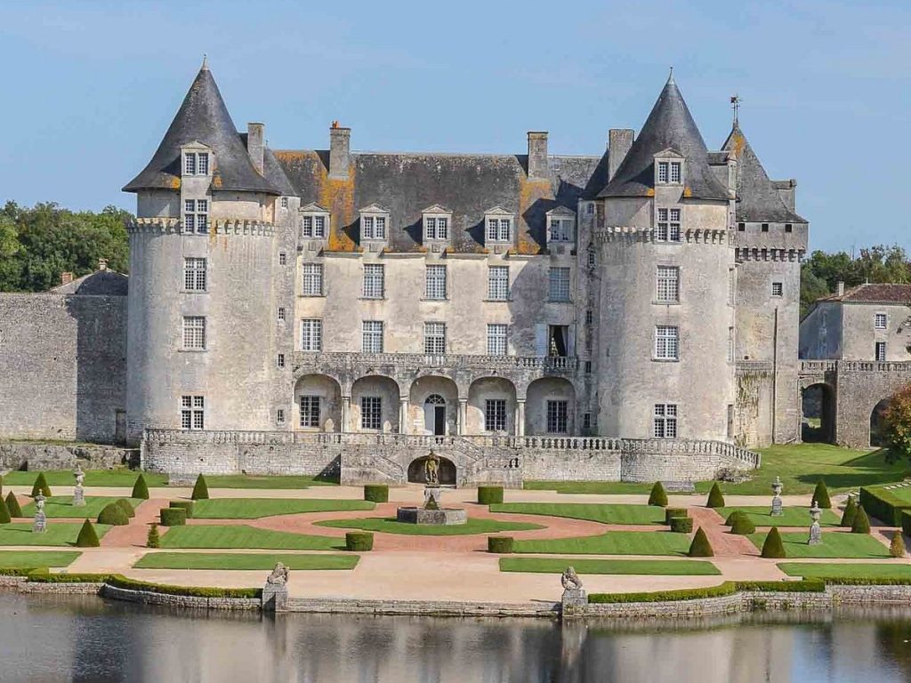 A castle with round towers above formal gardens and a moat