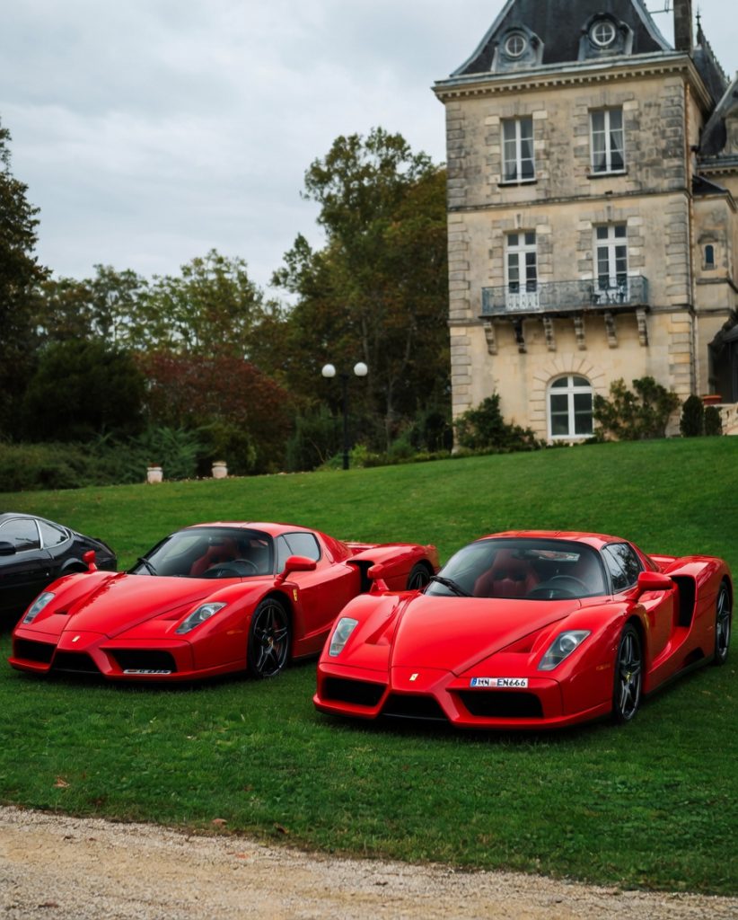 Two red sports cars on the lawn beside a château tower