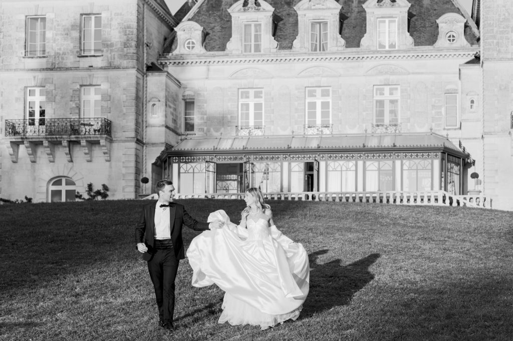 A bride and groom walking across the lawn in front of the château, in black and white