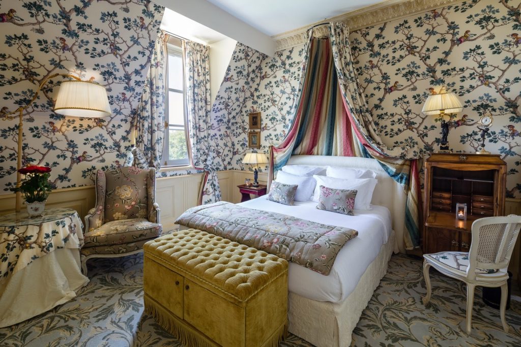 A Deluxe Room with floral wall fabric and a canopy bed