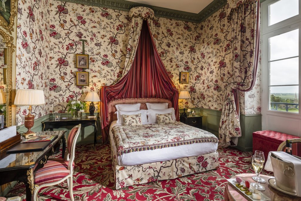 A Deluxe Room with red floral fabrics and a canopy bed