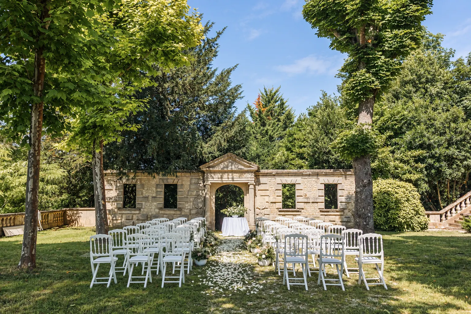 Ceremony chairs on the lawn beneath the plane trees, facing a stone arch