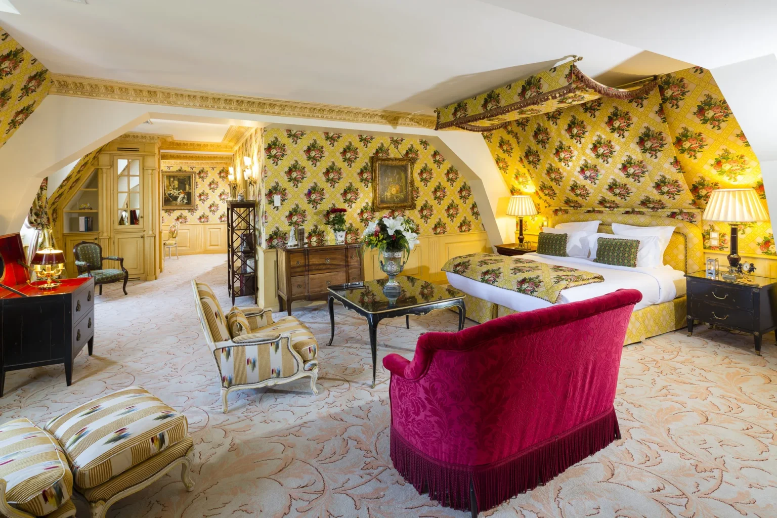 The Grand Suite with a large bed, yellow patterned walls and a red velvet sofa