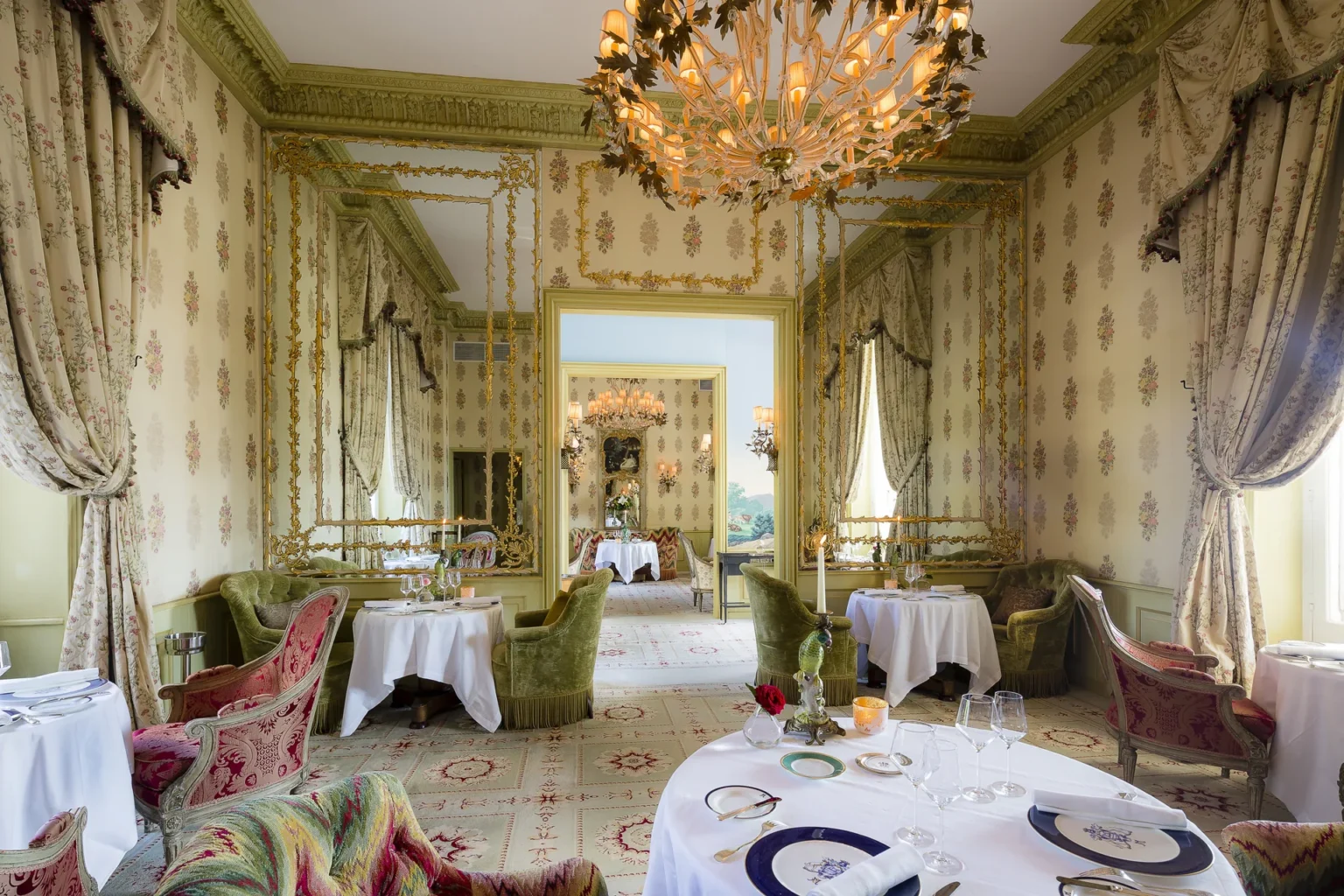 The Dining Room with a chandelier and round tables laid with white linen