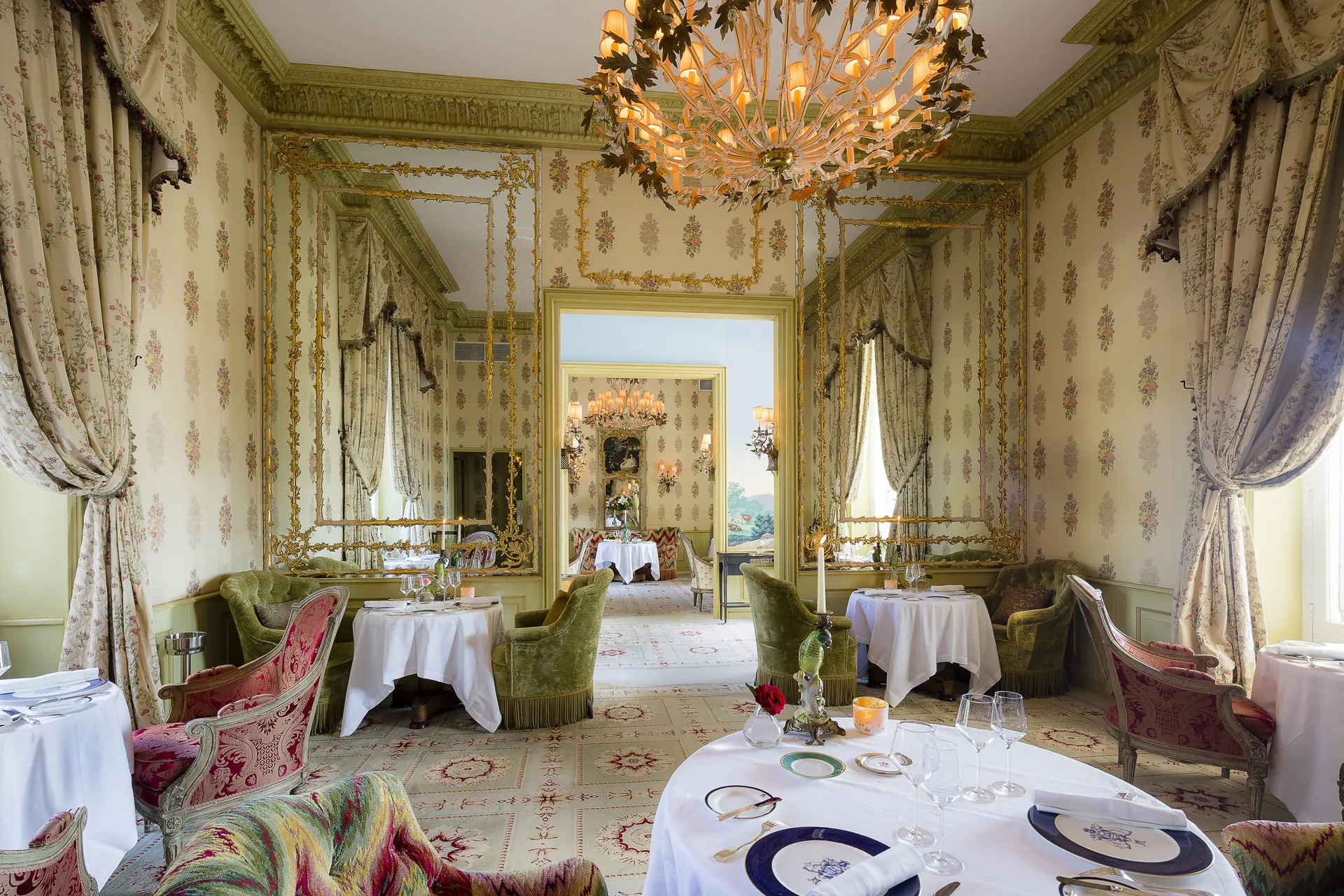 The Dining Room with a chandelier and round tables laid with white linen