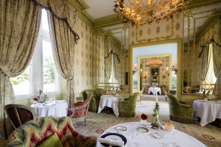 The Dining Room with a chandelier, set tables and tall draped windows