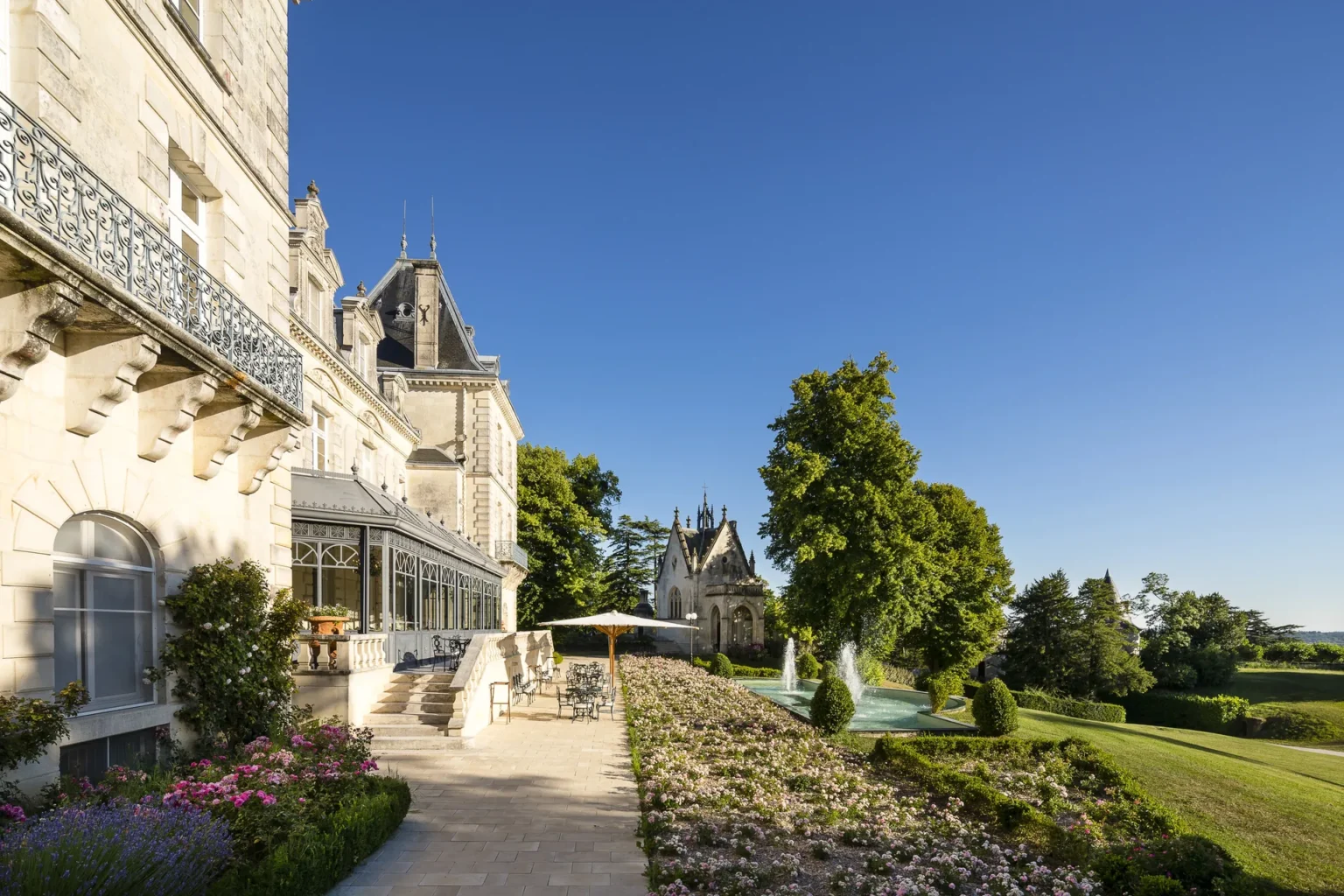 The garden terrace of the château with flower beds, a fountain and the park beyond