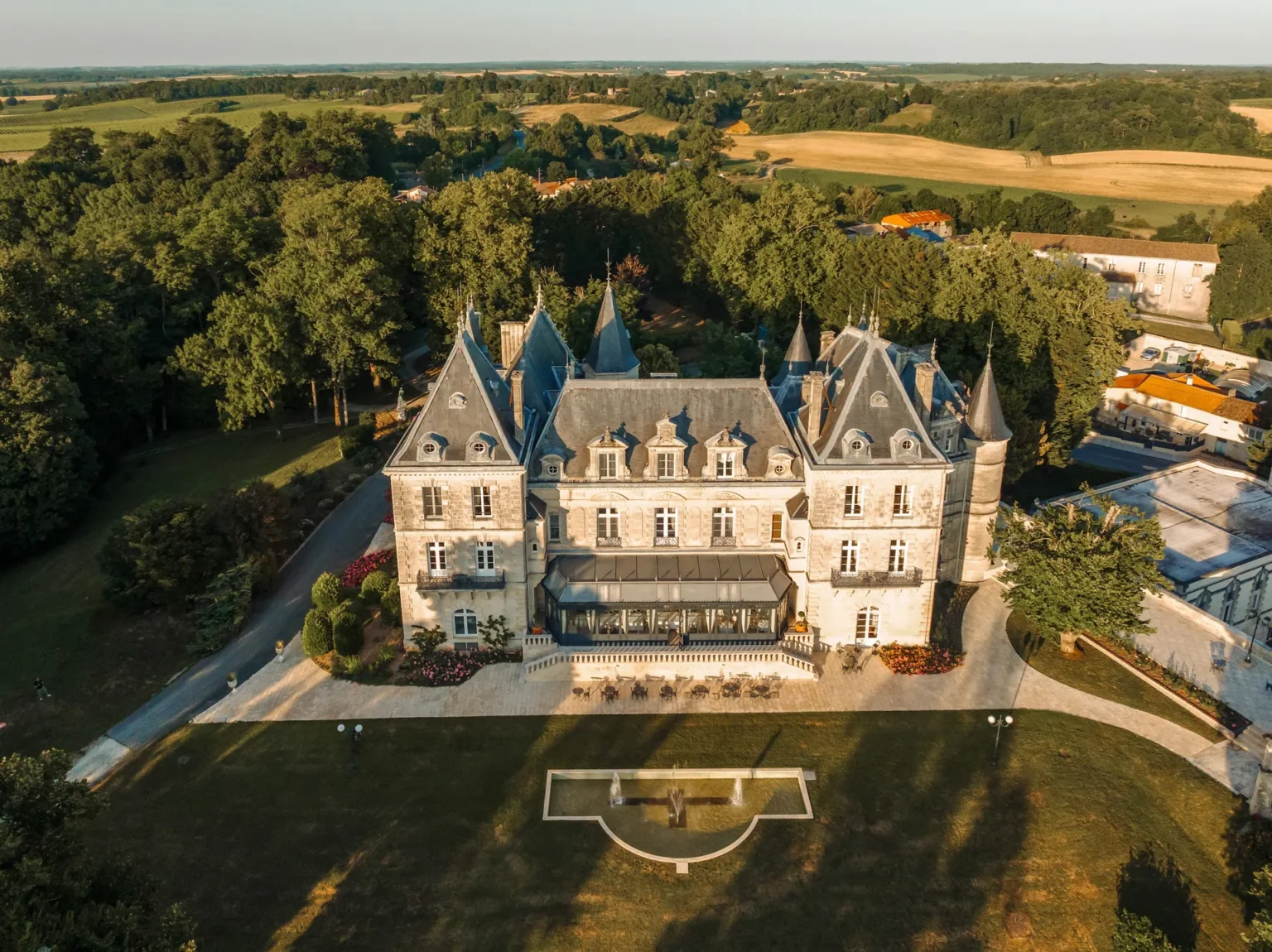 Aerial view of the château and its park in evening light, with the countryside beyond