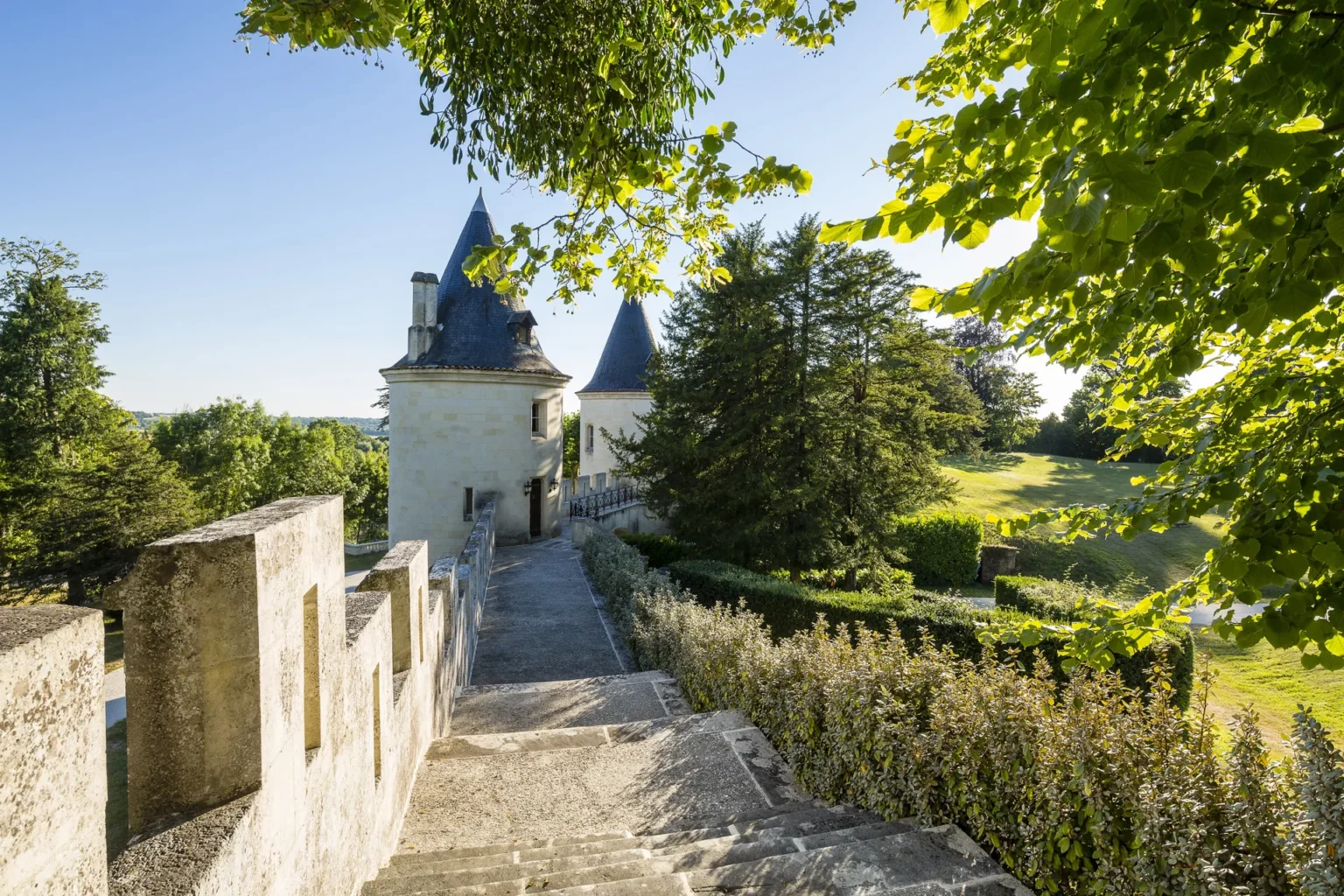 A stone rampart walk leading towards one of the château towers among trees