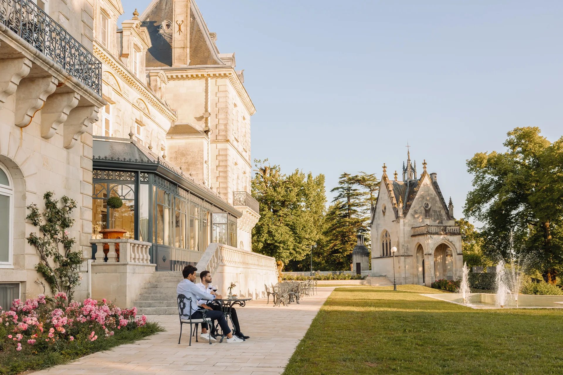 Guests seated on the garden terrace beside the glass veranda, with the chapel and park beyond