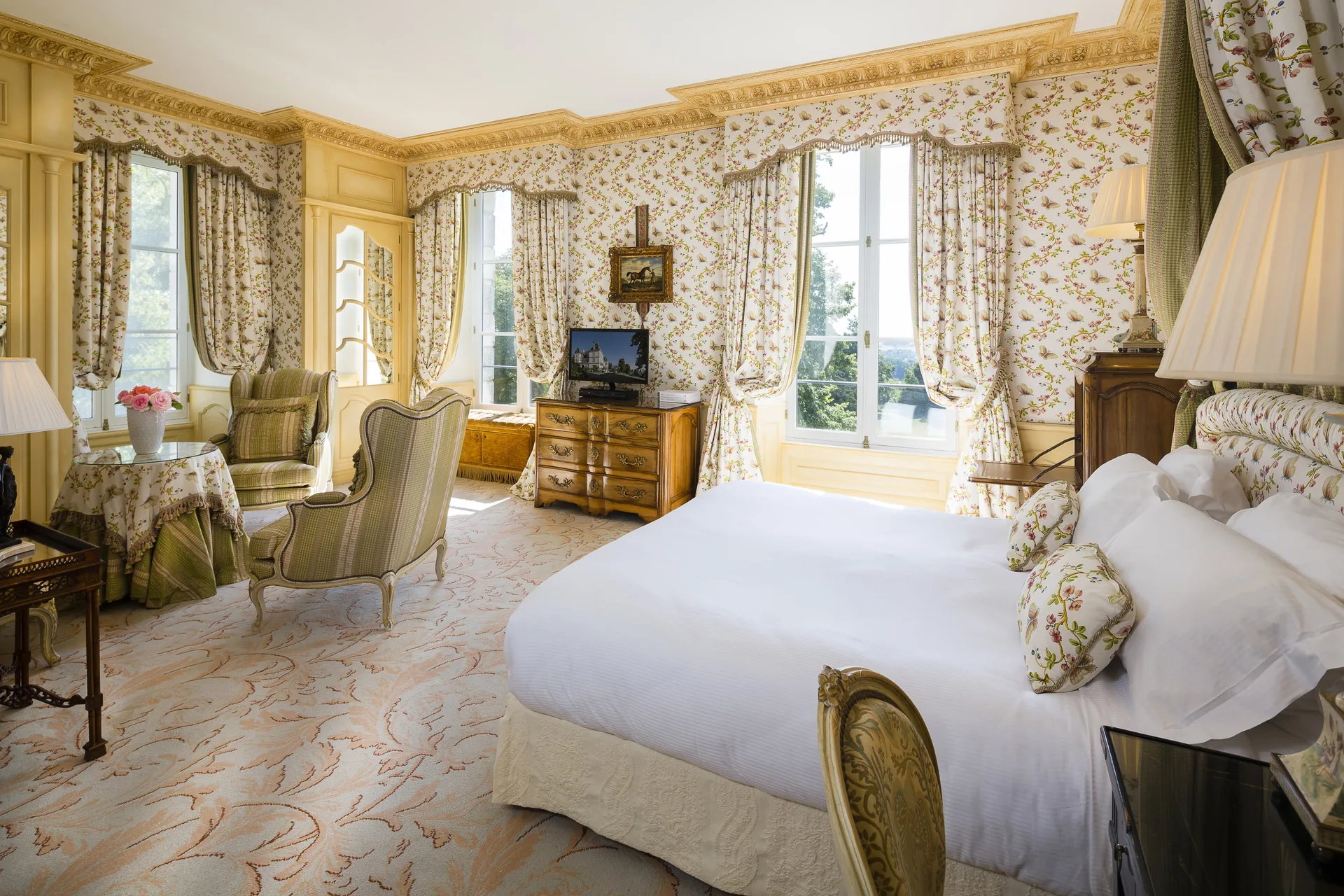A bright guest room with a large bed, armchairs and floral wall fabric