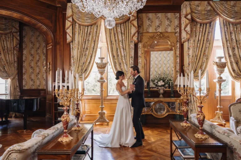 A couple posing in a wood-lined salon with a piano and candelabra