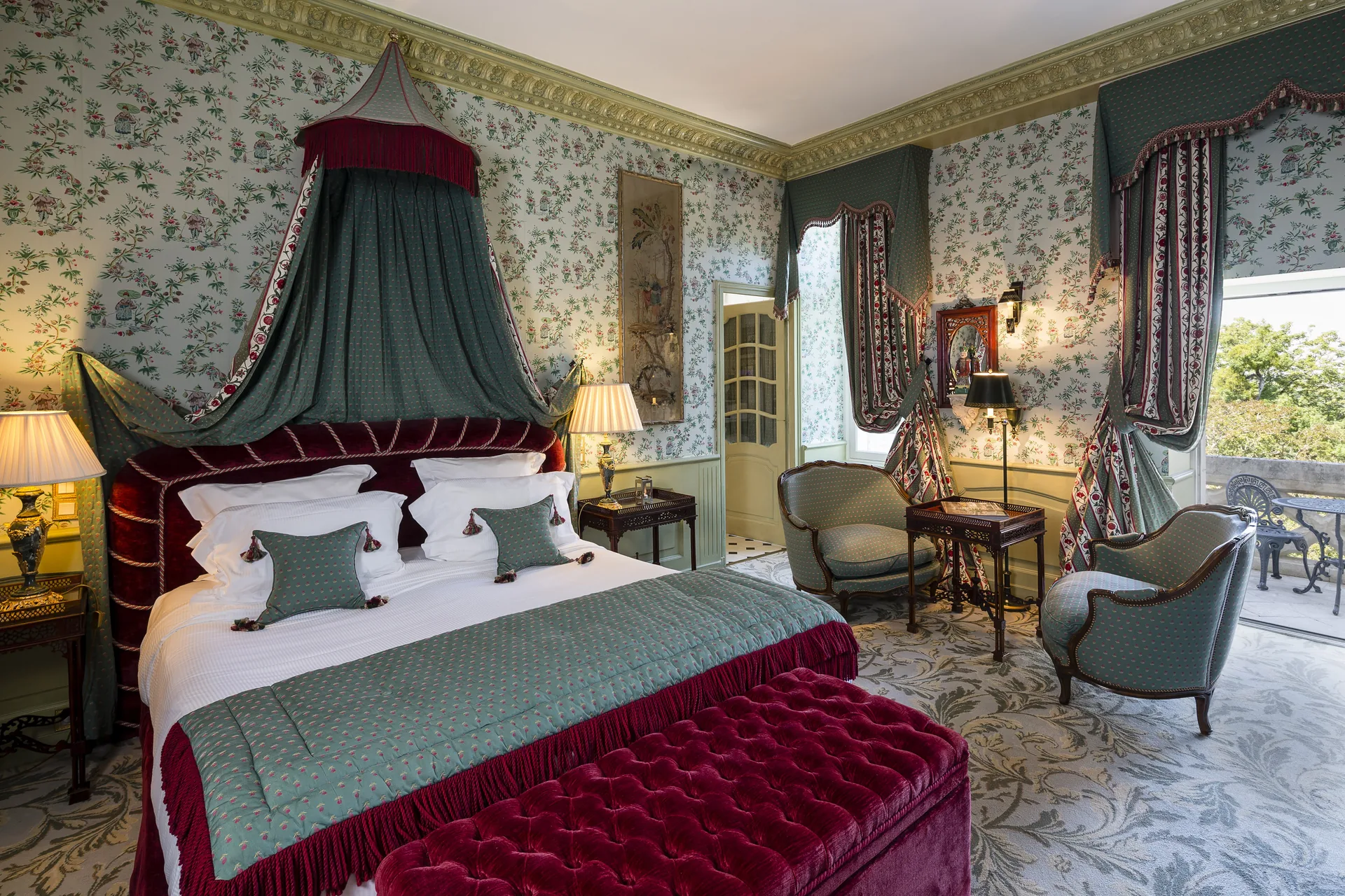 A bedroom with a canopy bed, floral wallpaper and a window opening onto the park