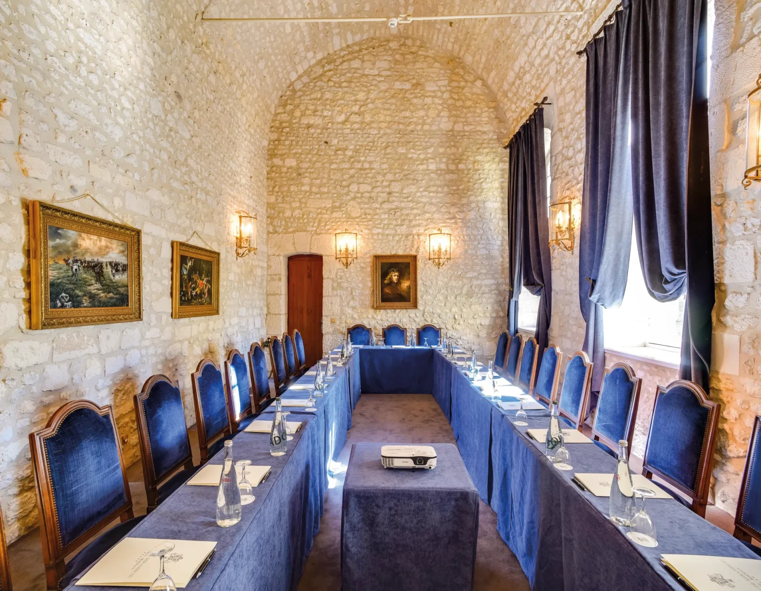 Salon Cognac set with a U-shaped table in a long stone room with windows along one side