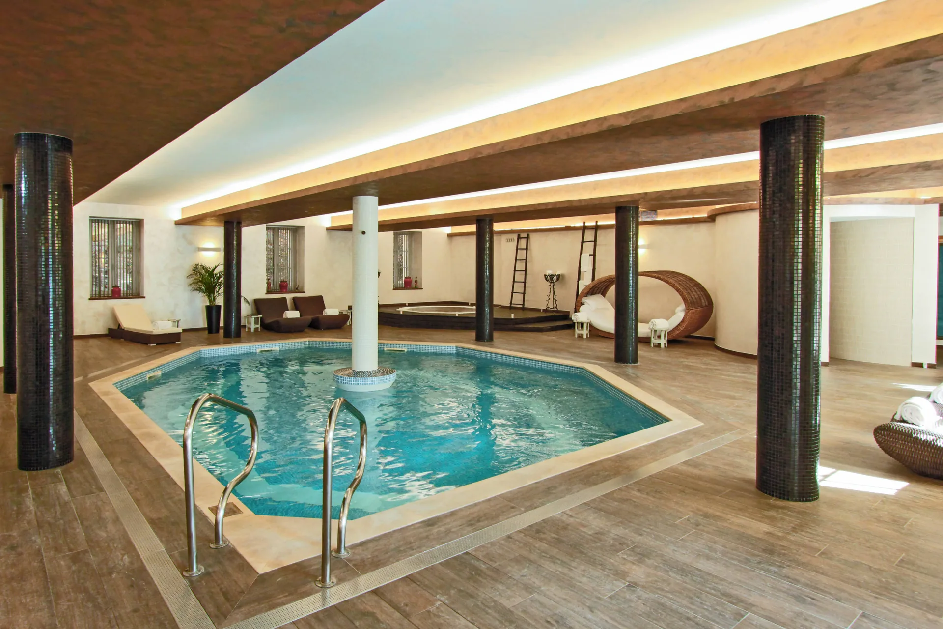 The indoor pool under a timber ceiling with loungers around it