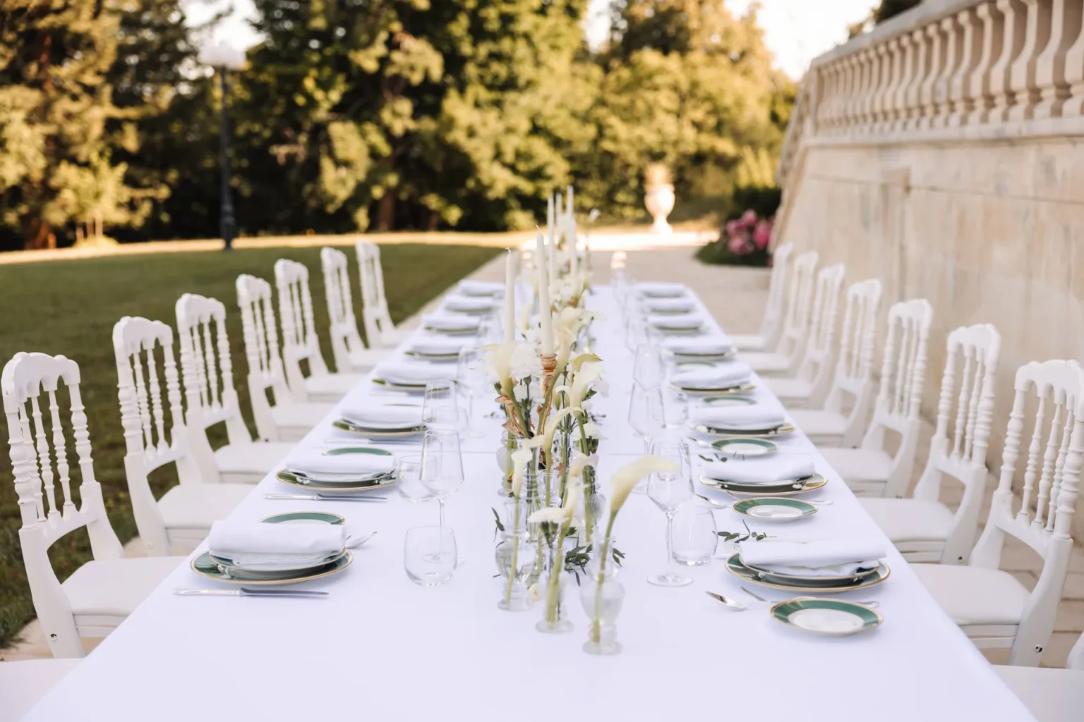 A long wedding table laid with white linen, glassware and flowers beside the château terrace