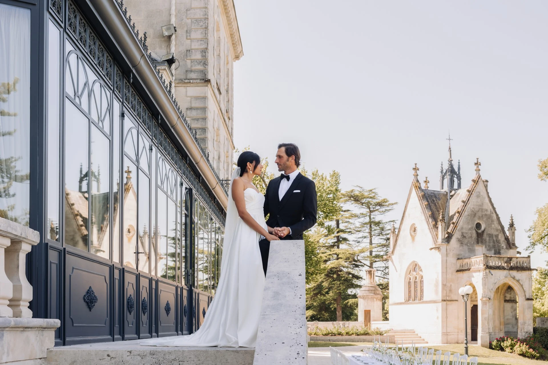 A bride and groom on the terrace beside the glass veranda, with the chapel behind